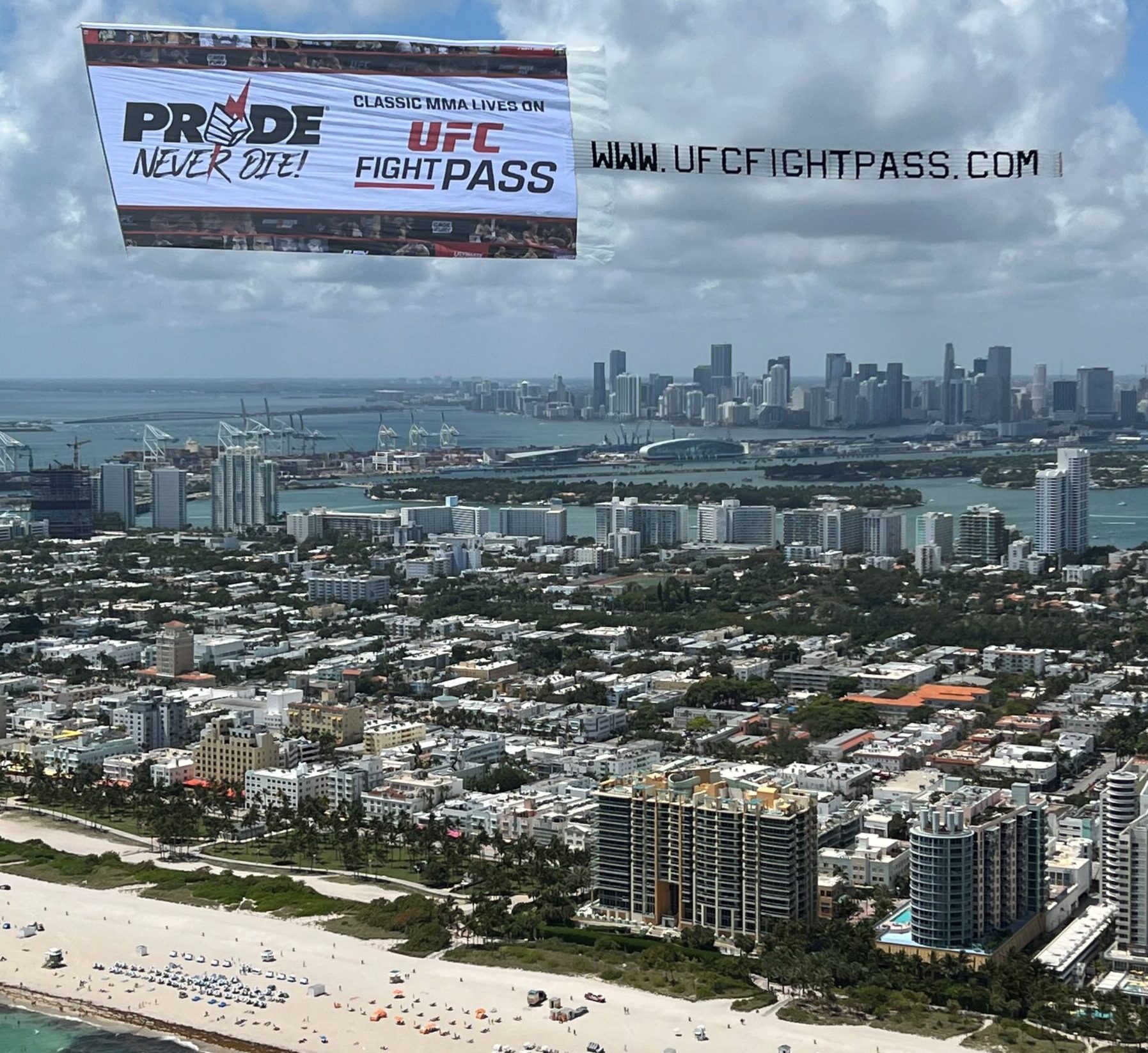 Aerial billboard and trailing letter banner flying over a crowded beach in South Florida to promote an upcoming UFC event.